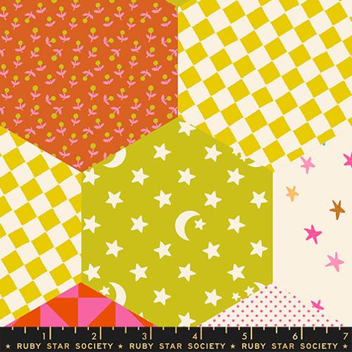 Fabric swatch with colorful patterns including stars, checkered, and geometric designs on a ruler for scale.