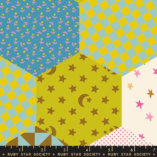 Fabric swatch with a patchwork pattern featuring stars, checkers, and other designs on a ruler at the bottom.