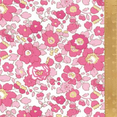 A close-up of a floral fabric pattern featuring pink and magenta flowers with yellow centers on a white background, with a gold metal ruler placed vertically on the right side for scale.