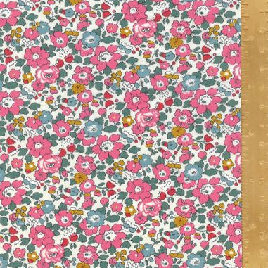 A close-up of a floral fabric pattern with pink, blue, and yellow flowers on a white background, with a wooden ruler along the right edge for scale.