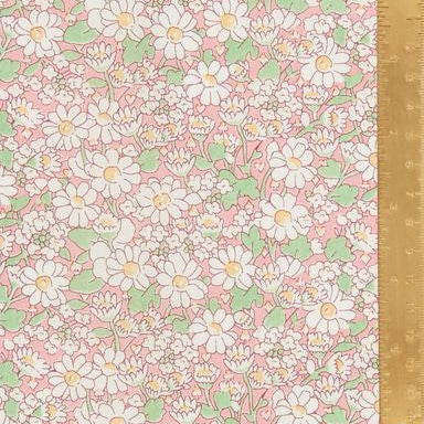 A close-up of a pink floral fabric or wallpaper pattern with white daisy-like flowers, green leaves, and small yellow centers, shown with a gold metal ruler along the right edge for scale.